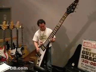 Man Playing Guitar In Front Of Guitar Shack Sign GIF
