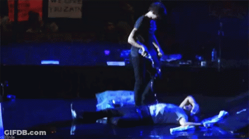 Man Playing Guitar While Another Man Laying On Stage GIF