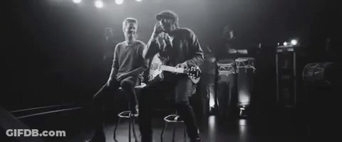 Man Playing Guitar While Another Sits On Bar Stool GIF