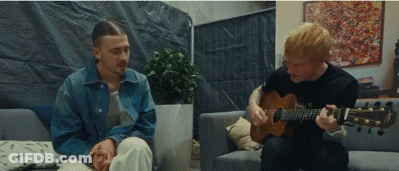Man Playing Guitar While Another Sits On Couch GIF