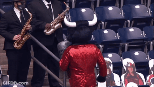 Man Playing Saxophone Next To Bull Mascot In Red Sequined Jacket GIF