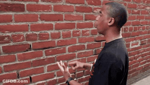 Man Pointing In Front Of Red Brick Wall GIF