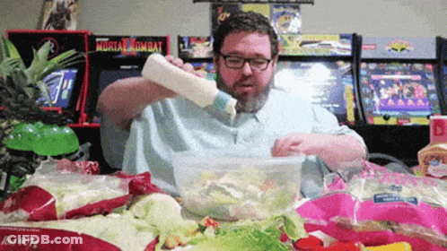 Man Pouring Dressing Into Salad In Front Of Mortal Kombat Arcade GIF
