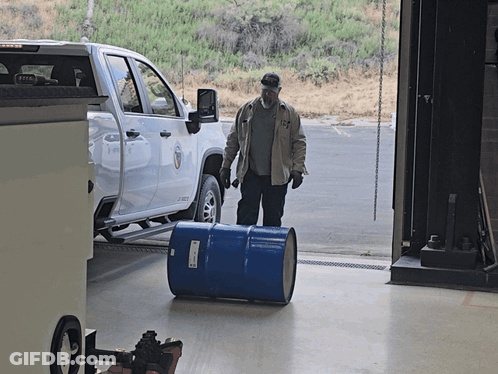 Man Pushing Blue Barrel In Front Of Ford Truck GIF