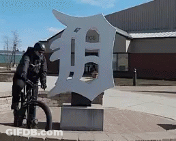 Man Riding Bike In Front Of Detroit Tigers Sign GIF