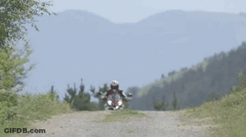 Man Riding Motorcycle On Dirt Road With Mountains GIF