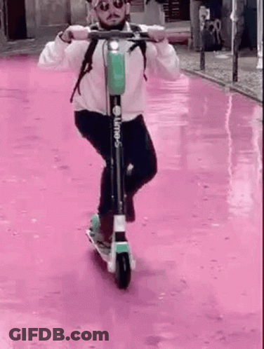 Man Riding Scooter Down Pink Street GIF