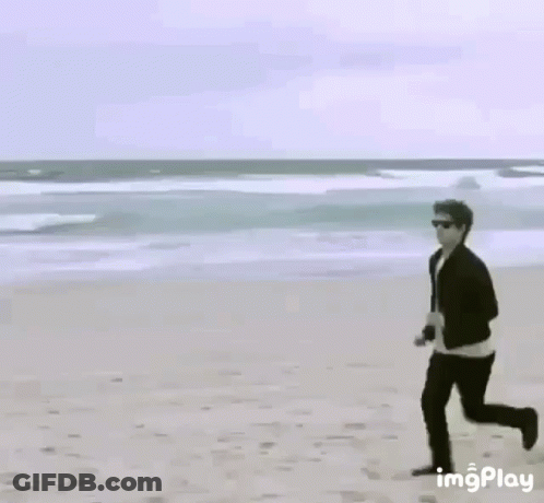 Man Running On Beach Next To Yellow Sign GIF