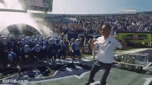 Man Running On Football Field With Players Behind Him GIF