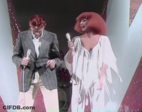 Man Singing Into Microphone Beside Woman In White Dress GIF