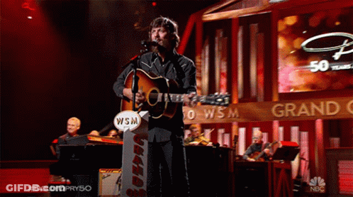 Man Singing Into Microphone Holding Guitar With WSM Sign GIF
