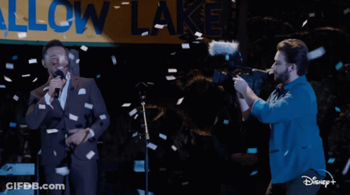 Man Singing Into Microphone In Front Of Allow Lake Sign GIF