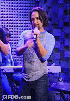 Man Singing Into Microphone In Front Of Blue Wall GIF