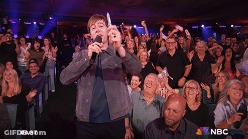 Man Singing Into Microphone In Front Of Crowd With NBC Logo GIF