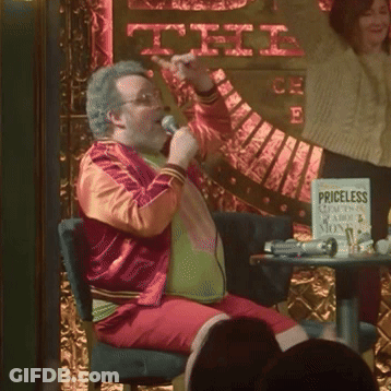 Man Singing Into Microphone In Front Of Priceless Sign GIF
