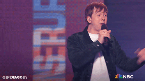 Man Singing Into Microphone In Front Of Saturn Sign GIF