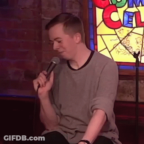 Man Singing Into Microphone In Front Of Stained Glass Window With Letter C GIF