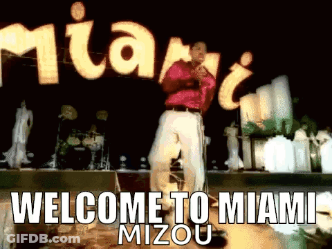 Man Singing Into Microphone In Front Of Welcome To Miami Sign GIF