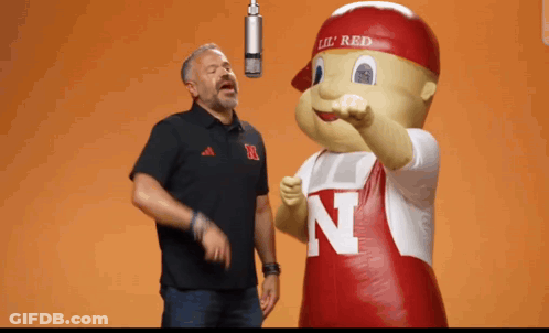 Man Singing Into Microphone Next To Mascot With Letter N GIF