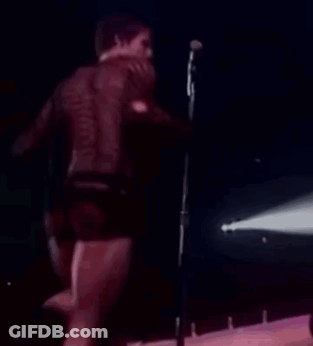 Man Singing Into Microphone On Stage In Shorts GIF