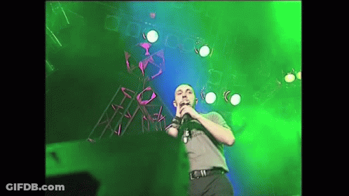 Man Singing Into Microphone On Stage With Green Lights GIF