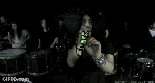 Man Singing Into Microphone With Drummers GIF