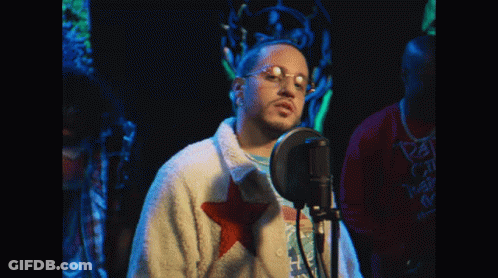 Man Singing Into Microphone With Glasses And White Jacket With Red Star GIF