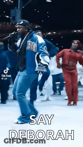 Man Singing Into Microphone With People Dancing Behind GIF