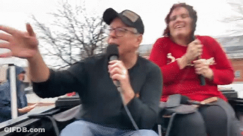 Man Singing Into Microphone With Woman Behind GIF