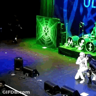 Man Singing On Stage With Microphone And Drum Set GIF