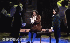 Man Sitting At Desk On Stage In Dark Room GIF