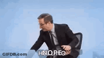 Man Sitting At Desk With Finger To Lips GIF