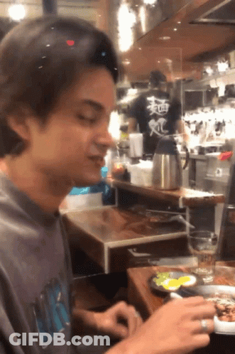 Man Sitting At Table With Food And Chinese Writing GIF