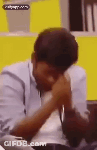 Man Sitting At Table With Hands On Face And Yellow Wall GIF