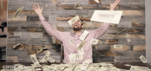 Man Sitting At Table With Money Falling From Sky GIF