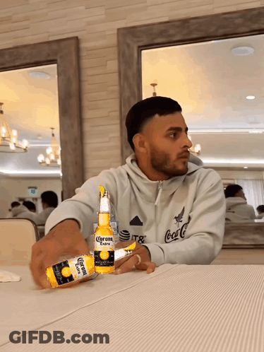 Man Sitting At Table With Two Corona Bottles GIF