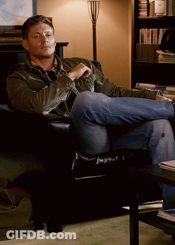 Man Sitting Cross-Legged In Chair Before Bookshelf GIF