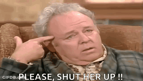Man Sitting In Chair With Finger To Forehead Asking To Shut Her Up GIF