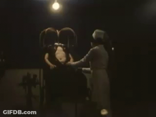 Man Sitting In Chair With Nurse In Dark Room GIF