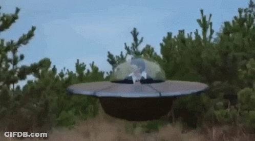 Man Sitting In Flying Saucer In Field GIF