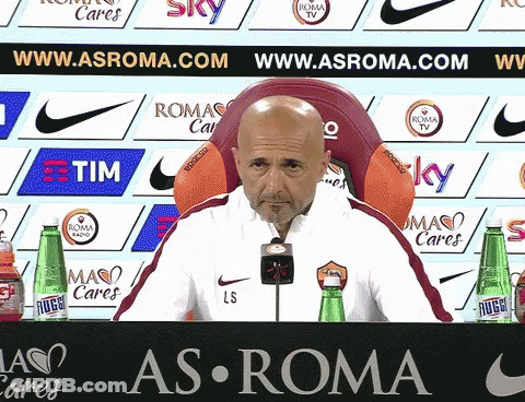 Man Sitting In Front Of As Roma Sign GIF