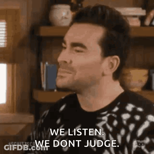 Man Sitting In Front Of Bookshelf Saying We Listen We Don't Judge GIF