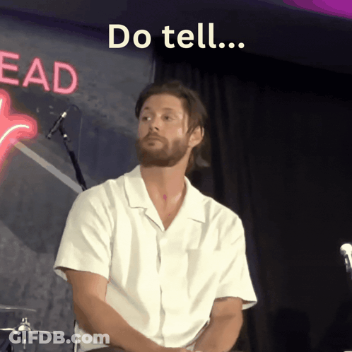 Man Sitting In Front Of Do Tell Neon Sign GIF