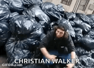 Man Sitting In Front Of Pile Of Trash Bags GIF