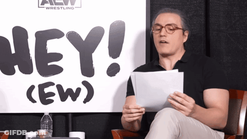 Man Sitting In Front Of Sign Saying Hey GIF