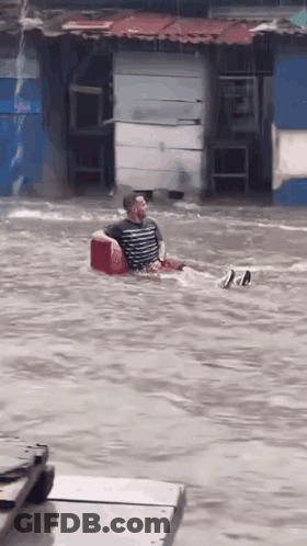 Man Sitting In Red Cooler In Flooded Street GIF