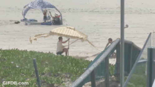 Man Sitting On Beach Holding Yellow And White Umbrella GIF