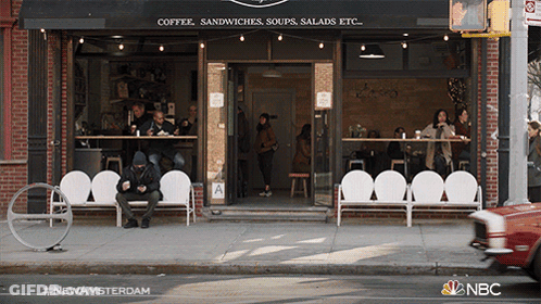 Man Sitting On Bench In Front Of Coffee Shop GIF