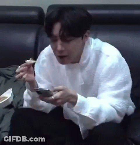Man Sitting On Couch Eating And Looking At Phone GIF