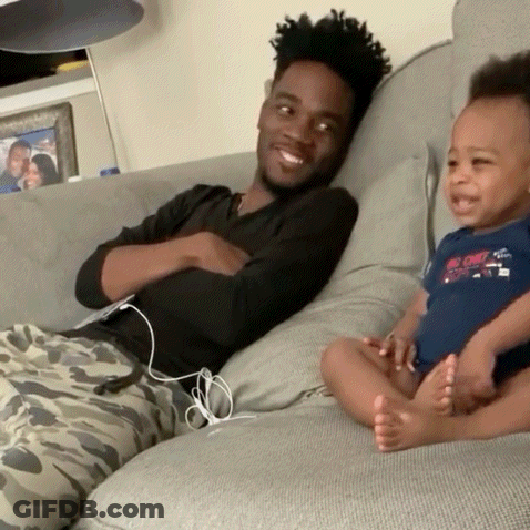 Man Sitting On Couch Holding Baby With Big Chill Shirt GIF